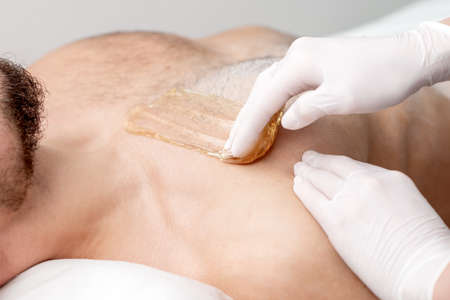 Epilation chest of young male with liquid wax paste by hands of female cosmetologist in beauty salonの写真素材