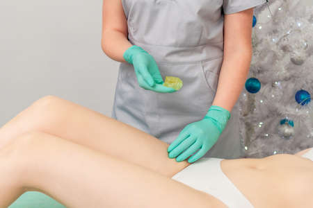 Cosmetologist in gloves applying paste for sugaring depilation on legs of young woman. Christmas discount waxingの写真素材