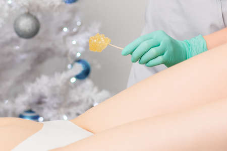 Young woman getting wax epilation of legs. Depilation concept. Product waxing bowl. Christmas...