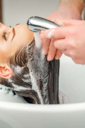 Close up of hands of hairdresser washing hair of woman in sink at beauty salonの写真素材
