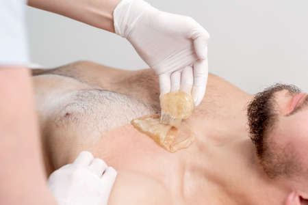 Epilation chest of young male with liquid wax paste by hands of female cosmetologist in beauty salonの写真素材