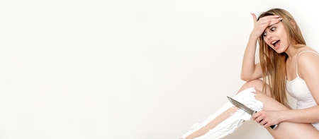 Beautiful young caucasian woman shaves her legs with a knife on a white backgroundの写真素材