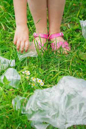 Hand of child cleans green grass from plastic trash in the parkの写真素材
