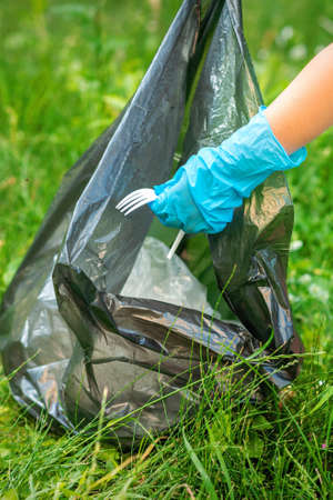 Child collects plastic trash from grass throwing garbage in garbage bag in the parkの写真素材