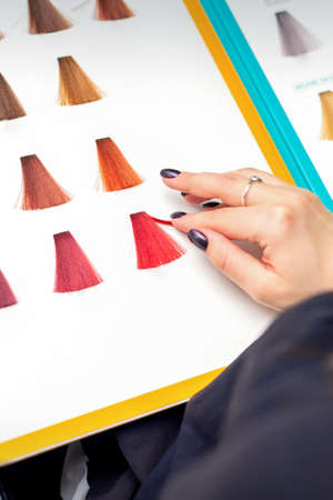 Customer's female hand choosing pink or red colour for hair colouring before hair dyeing in hair salonの写真素材
