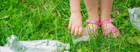 Hand of child cleans green grass from plastic trash in the parkの写真素材