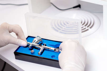 Close up shot of manicure master hand is taking out new clean airbrush tool for nails wearing gloves from the blue boxの写真素材