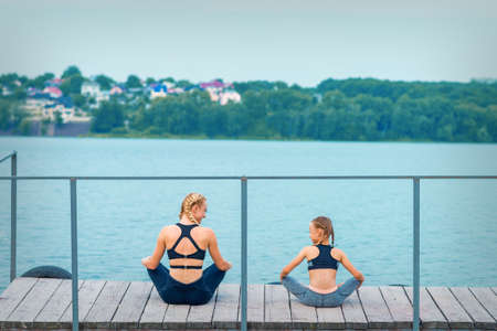 Mother and daughter doing gym exercises on the grass at the pier of the riverの写真素材