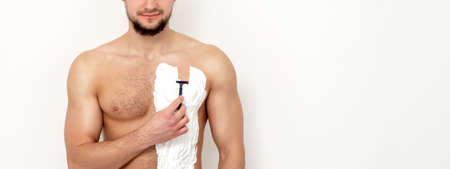 Young caucasian man with beard holds razor shaves his chest with white shaving foam on white background. Man shaving his torsoの写真素材