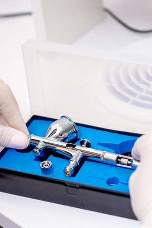 Close up shot of manicure master hand is taking out new clean airbrush tool for nails wearing gloves...