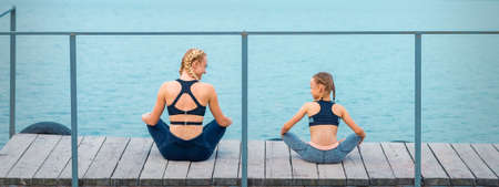 Mother and daughter doing gym exercises on the grass at the pier of the riverの写真素材