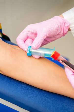 Nurse on pink gloves takes blood sample from vein from female patient in medical laboratory