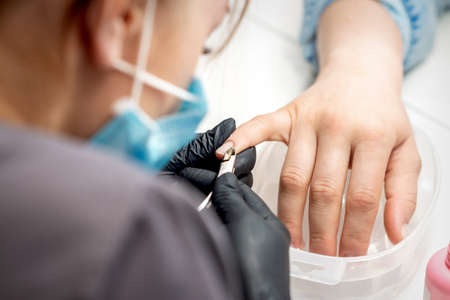 Manicure master removes cuticles by professional nail clipper metal tool on female nails in nail salonの写真素材