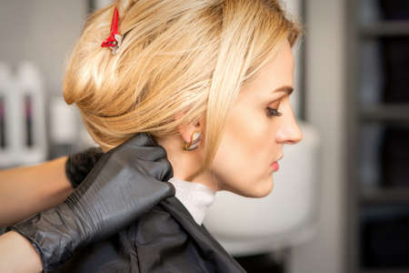 Hands of hairdresser making preparation before giving haircut to young blond woman at beauty salonの写真素材