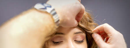 Front view of male hairdresser checks curly hairstyle of young caucasian woman in hair salonの写真素材