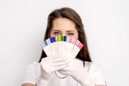 Portrait of female manicure master covering her face with nail sample palette on white backgroundの写真素材