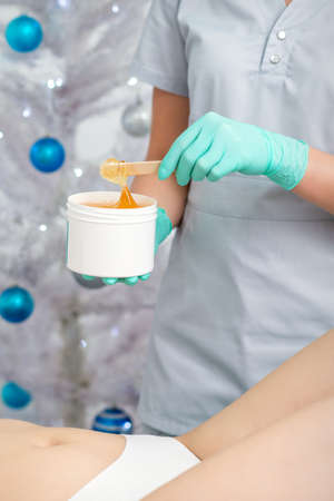 Female cosmetologist holding white blank jar with sugaring paste on christmas tree backgroundの写真素材