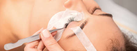 Young caucasian woman having eyelash extension procedure in beauty salon. Beautician glues eyelashes...