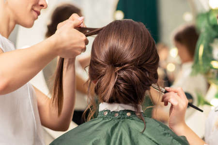Makeup artist and hairdresser are preparing hairstyle and visage of young woman in beauty salonの写真素材