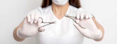 Manicure tools in hands of female manicurist wearing white mask and gloves on white background