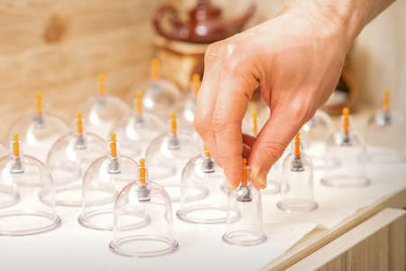 Masseur takes vacuum massage glass jars of traditional Chinese cupping therapy from table in spaの写真素材