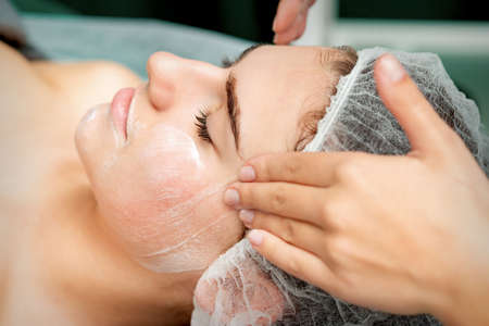 Young woman getting facial massage with closed eyes by beautician in beauty salonの写真素材