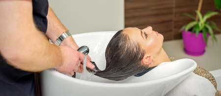 Male hairdresser rinses hair of young woman after shampooing at hair salonの写真素材