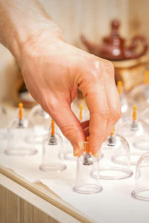 Masseur takes vacuum massage glass jars of traditional Chinese cupping therapy from table in spaの写真素材