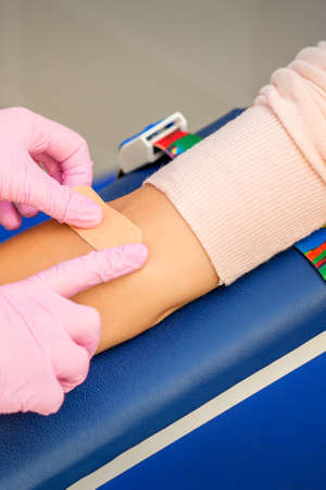 Close up of nurse hand applying adhesive plaster on arm of patient after blood collection in the hospitalの写真素材