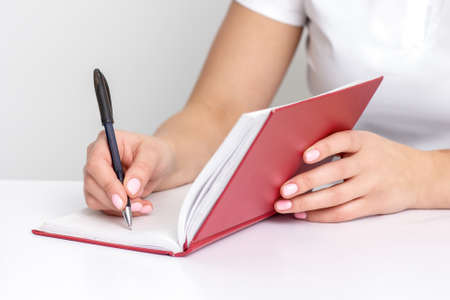 Young female hand writes notes to notebook planning her schedule at white table