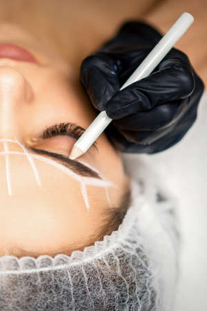 The beautician marks the eyebrow with a white pencil to prepare a permanent makeup procedureの写真素材