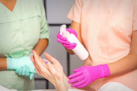Beautician in rubber protective gloves disinfects hands of woman with antiseptic spray in a beauty salonの写真素材
