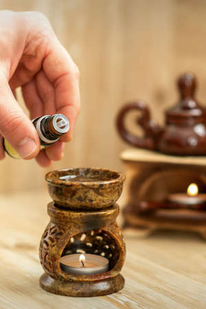 Hand of therapist pours drops of essential oil to ceramic diffuser in spa salon