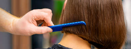 Rear view of male hairdresser combing short hair of woman in salonの写真素材