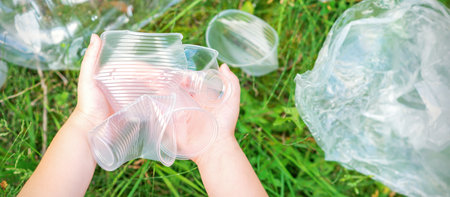 Childs hands clean the park from used plastic utensils in the grass
