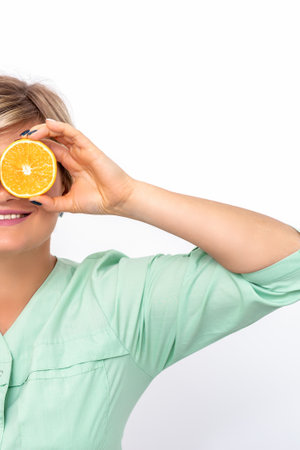 Cosmetologist or nutritionist covering the eyes with two halves orange fruit on a white backgroundの写真素材