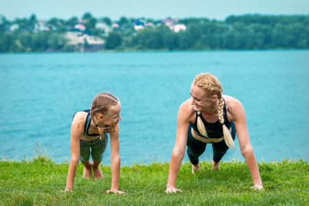 Woman and girl doing push-up exercise on the grass near lake outdoorsの写真素材
