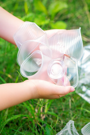 Childs hands clean the park from used plastic utensils in the grassの写真素材