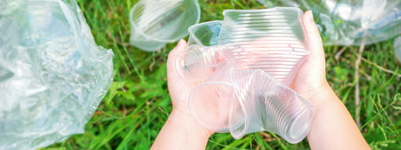 Childs hands clean the park from used plastic utensils in the grass