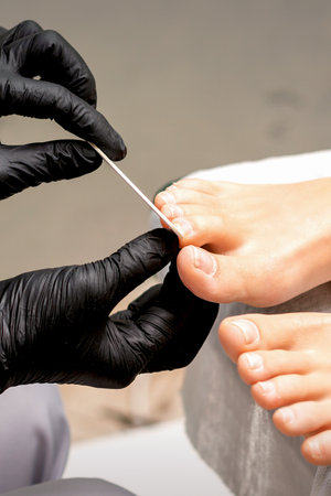 Pedicure master's hands in protective rubber gloves file female toenails with a nail file in a beauty salonの写真素材