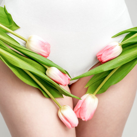 Bikini area of a young woman wearing a white underwear with pink tulips on white backgroundの写真素材