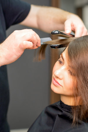 A male hairdresser is straightening the hair of the young woman in a beauty salonの写真素材