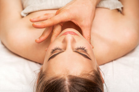 Chin or neck massage of a young woman by the hand of a male massage therapist in a spa salonの写真素材