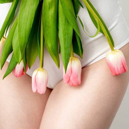 Bikini area of a young woman wearing a white underwear with pink tulips on white backgroundの写真素材