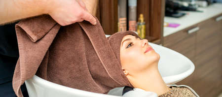 Hairdresser wraps female customer head with a towel in the sink at a hair salonの写真素材