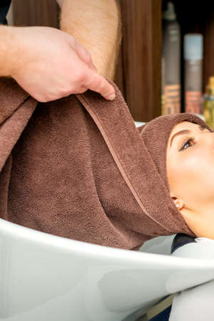 Hairdresser wraps female customer head with a towel in the sink at a hair salon