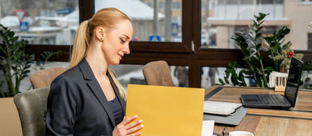 Young businesswoman looking at a folder with documents, while sitting at the table in a cafe