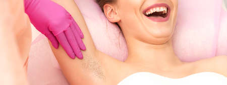Young woman during armpit examination before waxing procedure laughing in a beauty salon