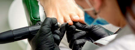 Pedicure master removes corns and cuticles with electric file machine on female toes in a nail salonの写真素材