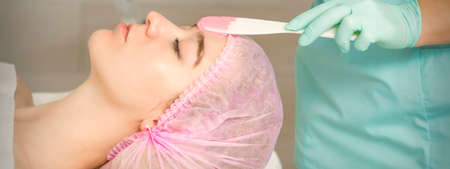 Close up of beautician's hand applying alginate mask on the face of the young caucasian woman in a...